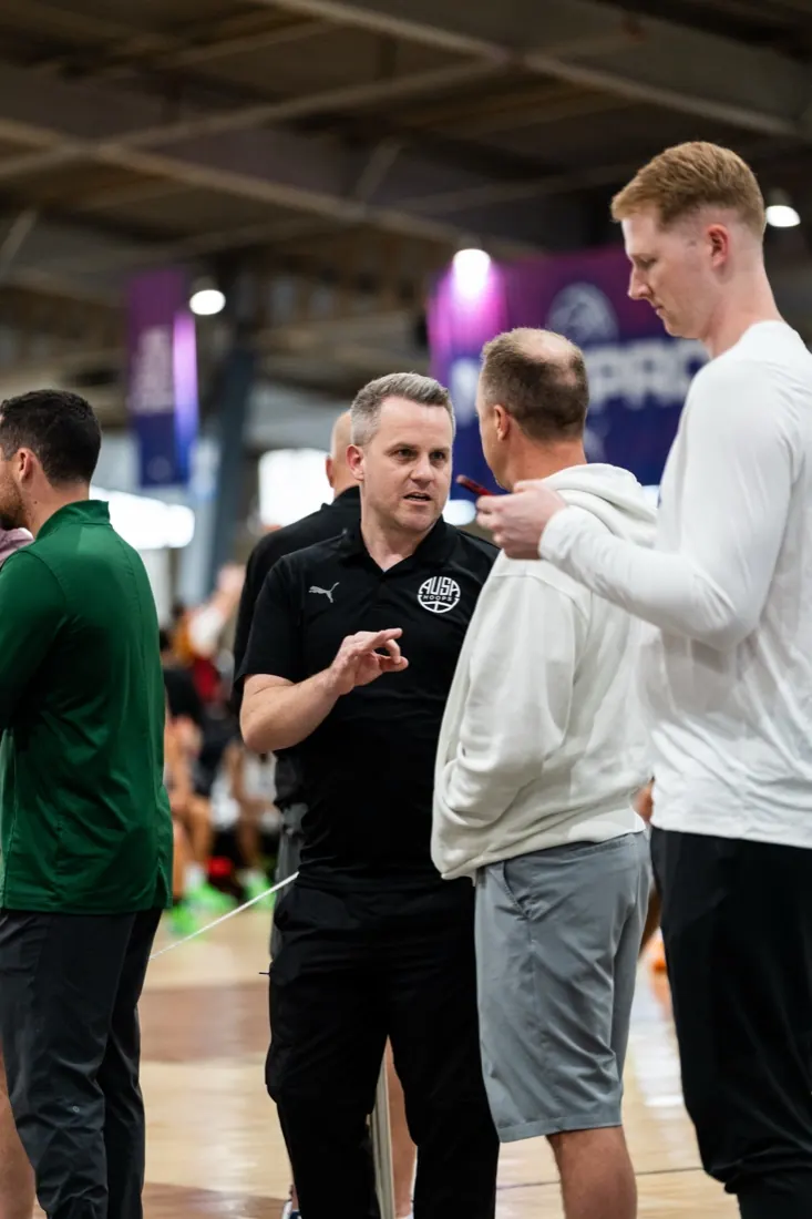 AUSA Hoops staff member in conversation with college coaches courtside at a US tournament