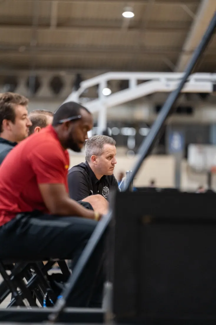 AUSA Hoops staff member seated among college coaches courtside at a US tournament