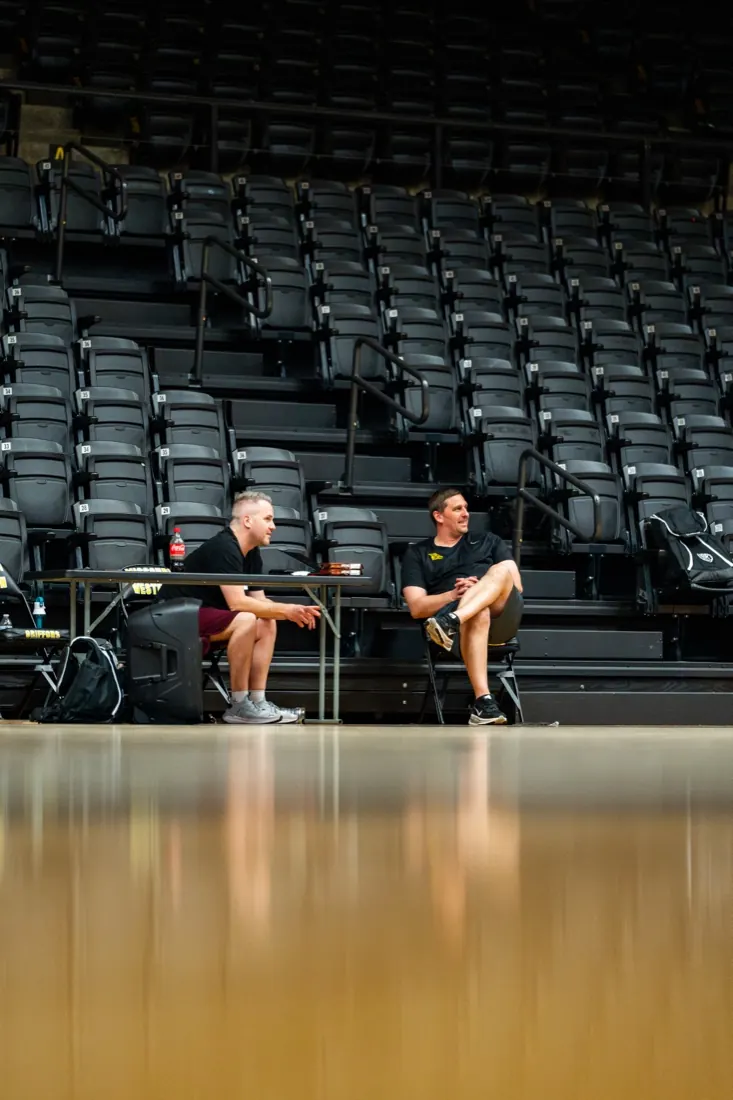Two AUSA Hoops staff working from a table courtside in an empty arena